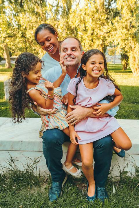 Mãe com duas filhas abraçadas novamente durante sessão fotográfica ao entardecer, retrato familiar com filhas rindo abraçadas à mãe, sessão lifestyle em ambiente natural ao ar livre'