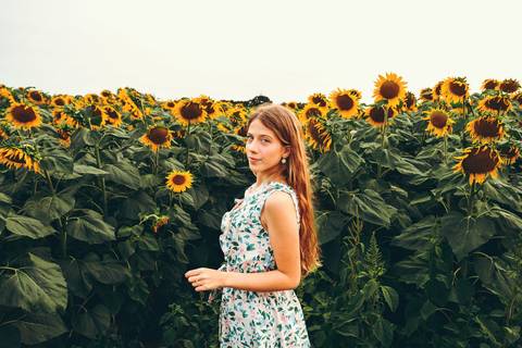 Mulher em retrato profissional com cabelo comprido, vestido floral em campo de girassol - Sess\u00e3o individual de fotografia profissional Duo Capuano, Riachos'