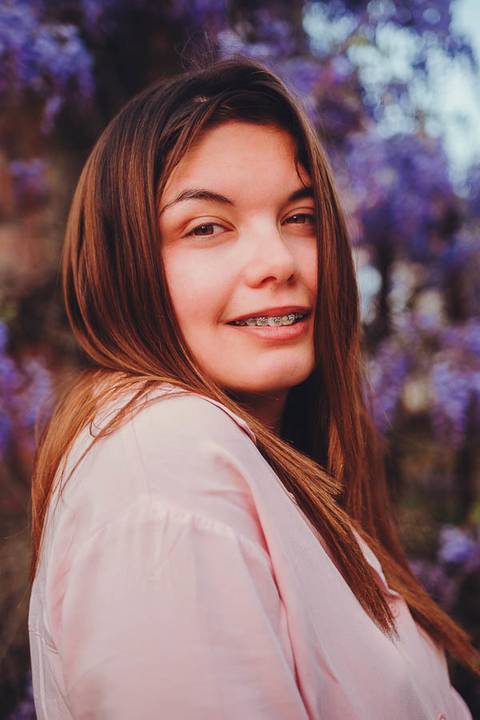 Retrato descontraído de Myriam Correia a sorrir com glicínias em flor ao fundo durante sessão fotográfica na Quinta da Cardiga, Golegã. Alegria e naturalidade num cenário primaveril. Duo Capuano.'