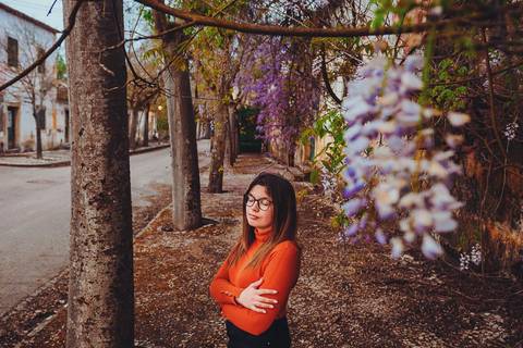 Myriam Correia de look laranja junto a árvores com glicínias durante sessão de retrato feminino na Quinta da Cardiga, Golegã. A cor vibrante em contraste com a beleza natural. Duo Capuano Fotografia.'