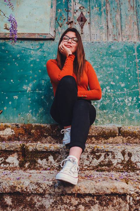 Myriam Correia de look laranja sentada junto a uma parede azul texturada durante sessão de retrato feminino na Quinta da Cardiga, Golegã. Cor e textura num equilíbrio visual perfeito. Duo Capuano.'