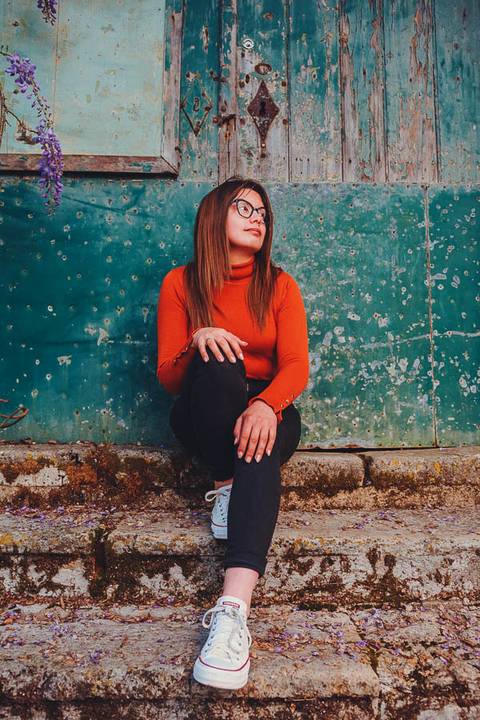 Myriam Correia de look laranja com expressão serena junto a parede azul durante sessão de retrato feminino na Quinta da Cardiga, Golegã. Elegância e autenticidade num retrato único. Duo Capuano.'