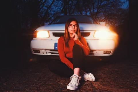 Myriam Correia sentada à frente do Seat Ibiza iluminada pelos faróis acesos durante sessão de retrato noturno na Quinta da Cardiga, Golegã. Uma imagem de impacto visual único. Duo Capuano Fotografia.'