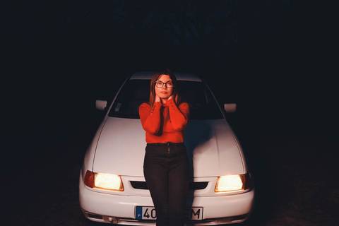 Myriam Correia em pose serena à frente do Seat Ibiza com faróis acesos durante sessão de retrato noturno na Quinta da Cardiga, Golegã. Luz dramática e expressão genuína. Duo Capuano Fotografia.'