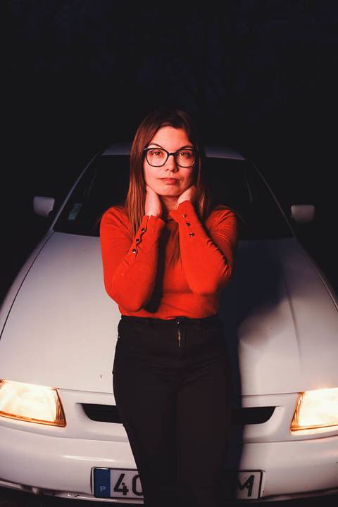 Myriam Correia com mãos no rosto em pose delicada durante retrato noturno junto ao Seat Ibiza na Quinta da Cardiga, Golegã. Um momento íntimo iluminado pela luz quente do carro. Duo Capuano.'