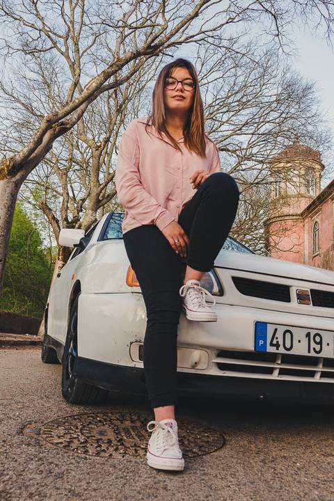 Myriam Correia sentada no capot do Seat Ibiza entre árvores floridas durante sessão de retrato feminino na Quinta da Cardiga, Golegã. A natureza e o carro como palco perfeito. Duo Capuano Fotografia.'