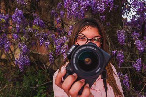Myriam Correia com câmara fotográfica rodeada de glicínias em flor durante sessão de retrato feminino na Quinta da Cardiga, Golegã. A fotógrafa retratada no seu elemento. Duo Capuano Fotografia.'