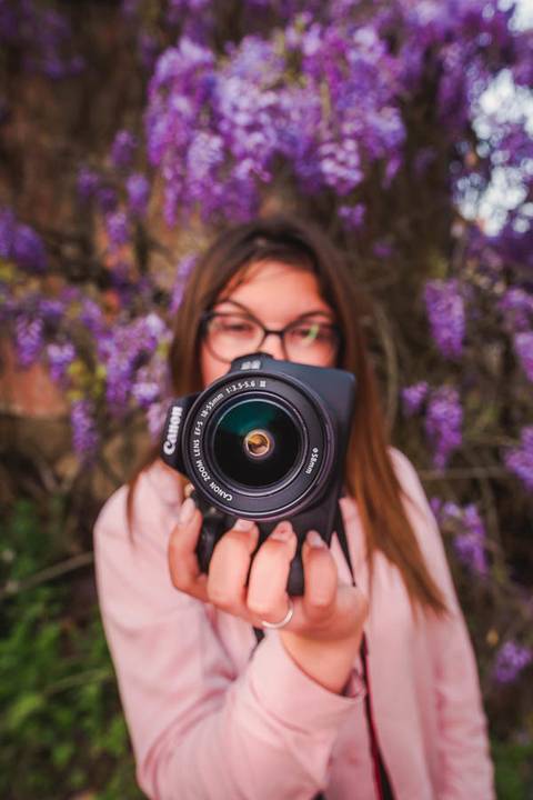 Myriam Correia com câmara fotográfica rodeada de glicínias em flor, revelando a sua paixão pela fotografia. Sessão de retrato feminino na Quinta da Cardiga, Golegã. Duo Capuano Fotografia.'