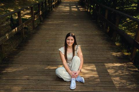 Retrato feminino sentada na ponte de madeira com sorriso natural – sessão fotográfica no Parque Verde do Bonito, Santarém, primavera'