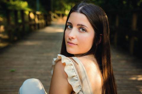 Sorriso delicado em retrato feminino sentada na ponte do Parque Verde do Bonito – sessão de retrato ao ar livre na primavera, Santarém'
