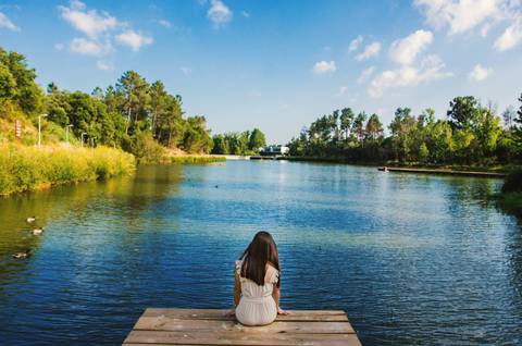 Mulher de costas sentada no pontão a contemplar o lago do Parque Verde do Bonito – retrato feminino em Entroncamento, Santarém'