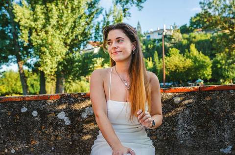 Susana em vestido branco junto a lago calmo com reflexo de árvores e céu azul. Pose natural e descontraída. Sessão fotográfica feminina individual ao ar livre em Torres Novas por Duo Capuano.'
