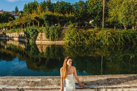 Susana em pose elegante junto ao lago em Torres Novas ao pôr do sol. Luz dourada, vestido branco e paisagem natural refletida na água. Sessão fotográfica feminina individual por Duo Capuano.'