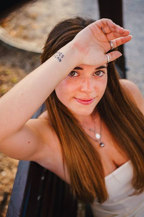Retrato feminino com cabelo ruivo ao vento e sorriso cúmplice. Susana posa descontraidamente com colar delicado. Sessão fotográfica individual ao ar livre em Torres Novas por Duo Capuano.'