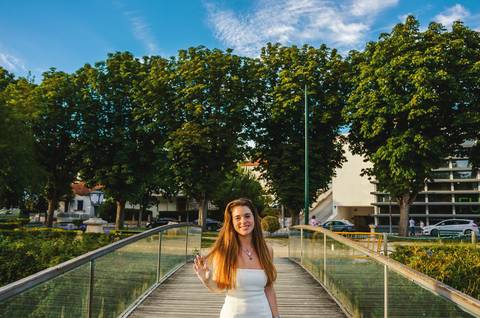Susana em vestido branco caminhando em passadiço de madeira junto ao lago. Fotografia feminina ao pôr do sol em Torres Novas com luz quente e vegetação exuberante. Sessão por Duo Capuano.'