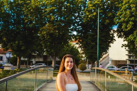 Susana em vestido branco a andar em passadiço de madeira ao pôr do sol em Torres Novas. Luz quente e ambiente urbano e natural. Fotografia feminina individual ao ar livre por Duo Capuano.'