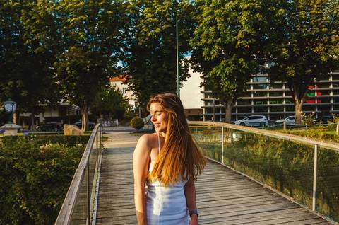 Susana em vestido branco com pose confiante em passadiço de madeira ao pôr do sol em Torres Novas. Luz quente e urbana ao entardecer. Fotografia feminina individual por Duo Capuano Fotografia.'