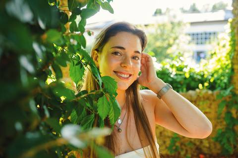 Fotografia de retrato ao ar livre com luz natural. Susana sorri entre vegetação exuberante do Jardim das Rosas, Torres Novas. Sessão fotográfica feminina individual por Duo Capuano.'