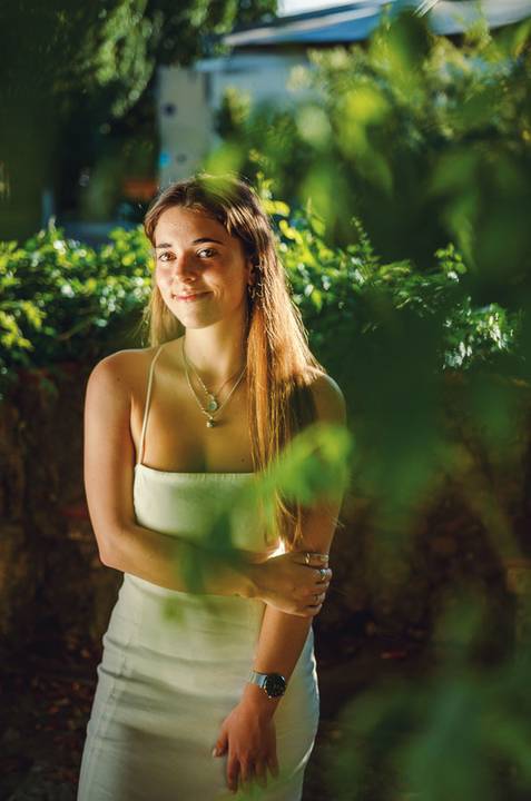 Sessão fotográfica feminina com top branco e pose descontraída. Susana enquadrada pela vegetação do Jardim das Rosas, Torres Novas. Fotografia individual ao ar livre por Duo Capuano.'