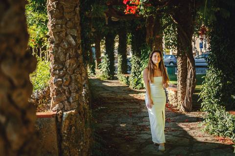 Fotografia de corpo inteiro em corredor de árvores no Jardim das Rosas, Torres Novas. Susana com vestido branco numa pose elegante e natural. Sessão fotográfica individual por Duo Capuano.'
