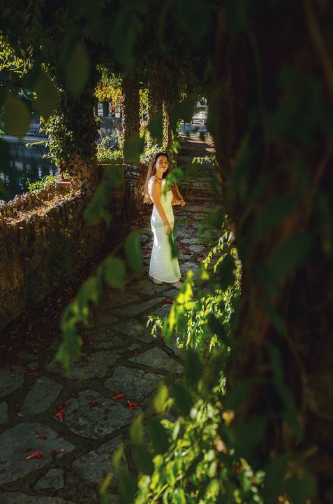 Sessão fotográfica feminina entre muros cobertos de trepadeiras no Jardim das Rosas, Torres Novas. Susana em vestido branco com pose graciosa ao ar livre. Fotografia individual Duo Capuano.'