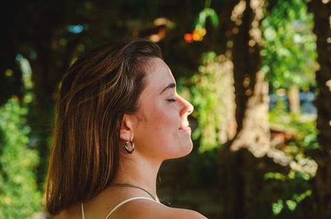 Retrato artístico de perfil com luz lateral suave e sombras naturais no jardim. Susana com olhar pensativo e cabelo ruivo solto. Sessão fotográfica feminina individual por Duo Capuano.'