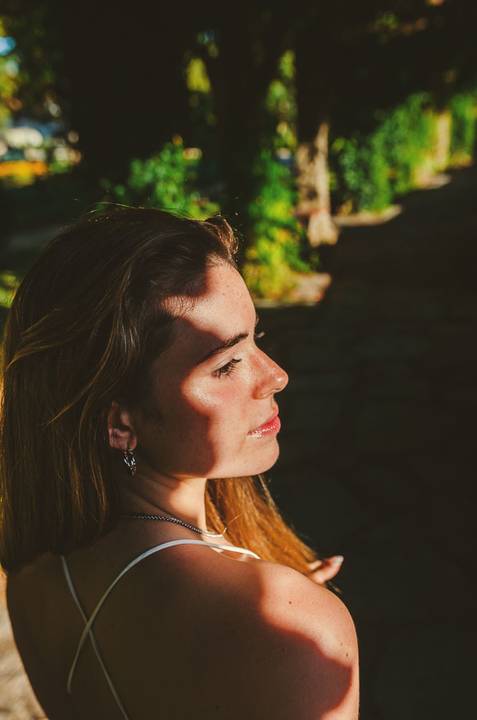 Fotografia artística de perfil feminino com luz lateral dourada. Sombras suaves e expressão contemplativa da Susana. Sessão individual no Jardim das Rosas, Torres Novas, por Duo Capuano.'