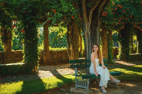 Susana sentada sob pérgola de árvores com luz filtrada e sombras em padrão geométrico. Fotografia feminina ao ar livre no Jardim das Rosas, Torres Novas. Sessão individual por Duo Capuano.'