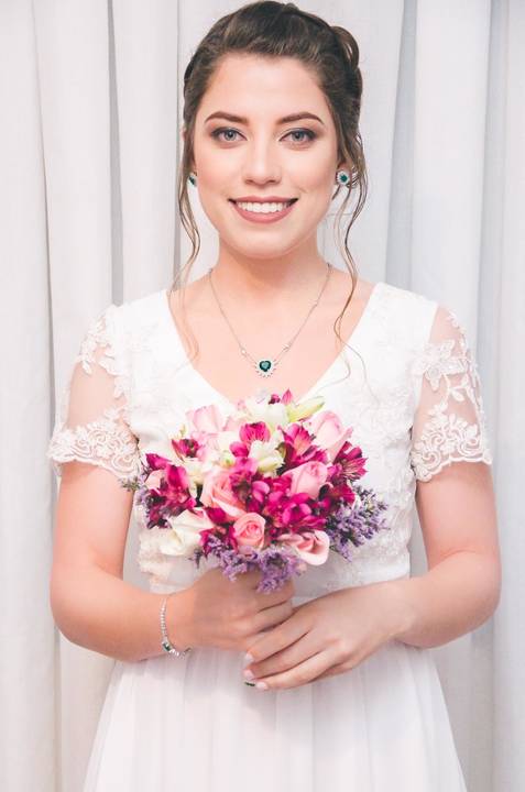 Noiva Camila sorrindo de frente em vestido branco de renda com buquê magenta para casamento em São Paulo, retrato frontal da noiva'