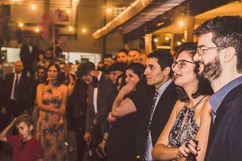 Casal Camila e Rafael dançando durante festa de casamento com convidados ao fundo em São Paulo, momento de diversão na pista'
