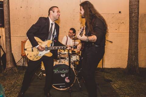 Músicos tocando guitarra e cantando durante banda ao vivo em casamento Camila e Rafael em São Paulo com iluminação ambiente'