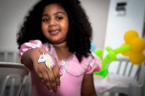 aniversariante feliz com a sua festa infantil no tema princesas com seu vestido lindo e sua tatuagem infantil de unicornio'