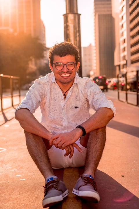 moda, luxo, ensaio masculino portrait do fotografo em sao paulo na avenida paulista sentado no meio da rua com seu look branco e  seus oculos no por do sol golden hour, cachos'