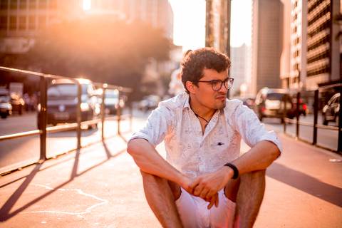 moda, luxo, ensaio masculino portrait do fotografo em sao paulo na avenida paulista sentado no meio da rua com seu look branco e  seus oculos no por do sol golden hour, cachos'