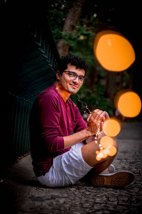 moda, luxo, ensaio masculino portrait do fotografo em sao paulo na avenida paulista sentado no meio da rua com seu look branco e  seus oculos no por do sol golden hour, cachos, luzes de fada'