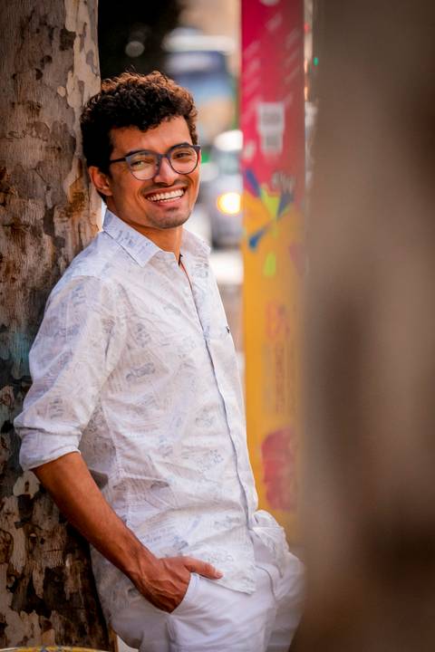 moda, luxo, ensaio masculino portrait do fotografo em sao paulo na avenida paulista sentado no meio da rua com seu look branco e  seus oculos no por do sol golden hour, cachos'