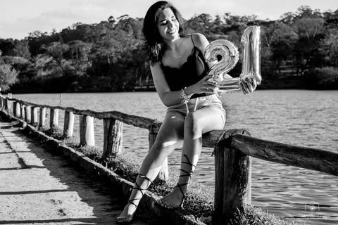 Aniversariante sentada no corrimão a beira de um lago no Parque do Carmo – Olavo Egydio Setúbal, localizado em São Paulo, comemorando o seu ensaio de 21 anos. Foto feita por Mary Santtiago de Suzano SP
'