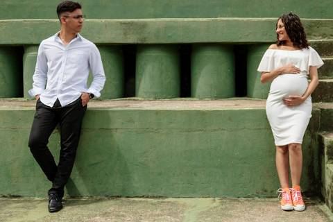 Casal em ensaio de gestante de pé olhando um para o outro'