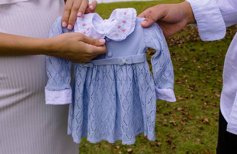 Casal segurando um vestido de bebê'