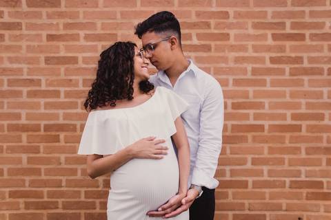 Casal em ensaio de gestante posando em parede de tijolinhos'