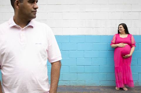 casal posando para foto de gestante. Mulher ao fundo e homem a frente'