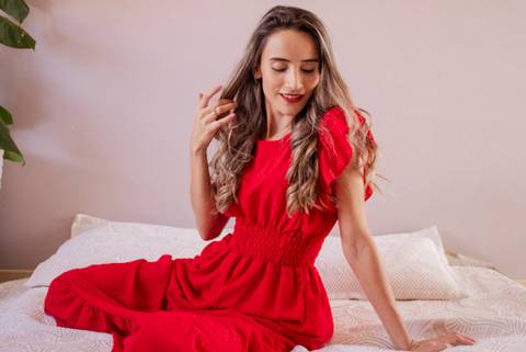 mulher de vestido vermelho sentada na cama segurando o cabelo em seu ensaio de aniversário. Foto de Mary Santtiago'