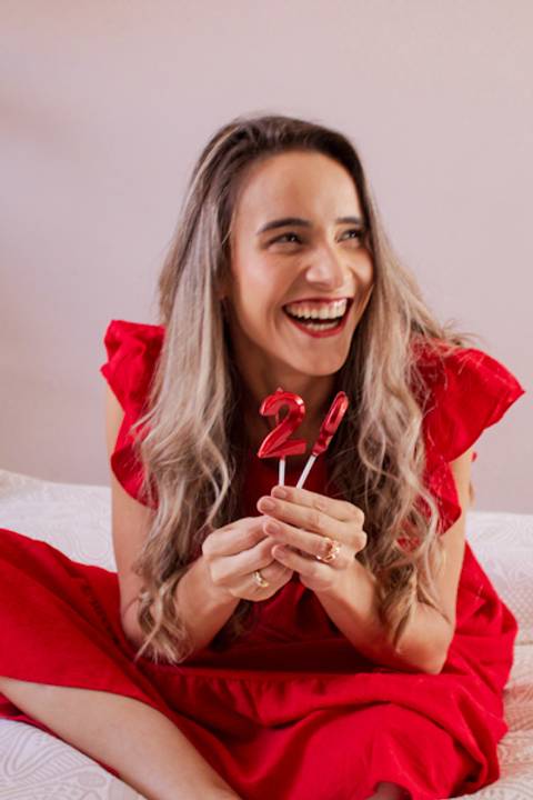 Mulher de vestido vermelho segurando velas de aniversário enquanto sorri foto de Mary Santtiago'