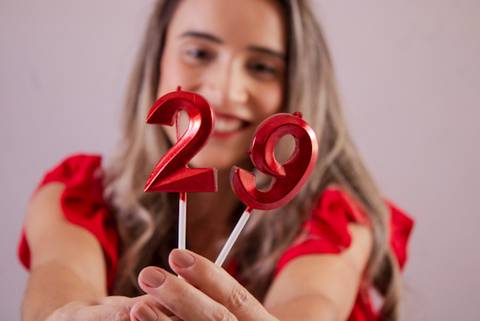 mulher segurando vela de aniversário enquanto sorri, com efeito desfocado. Foto de Mary Santtiago'