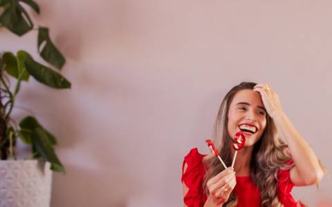 Mulher de vestido vermelho segurando vela de aniversário com uma composição bem descontraída. Foto de Mary Santtiago'