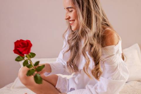 mulher segurando rosa vermelha enquanto sorri e posa para foto. Foto de Mary Santtiago'