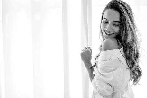 foto em preto e branca de uma mulher segurando uma cortina enquanto posa para uma foto de aniversário. Foto de Mary Santtiago'