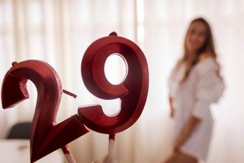Ensaio de aniversário , vela vermelha de 29 anos em destaque enquanto modelo posa ao fundo. Foto de Mary Santtiago'