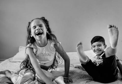 Foto descontraída de irmãos se jogando na cama durante um ensaio fotográfico'