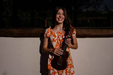 garota de vestido de estampa laranja encostada em uma parede sorrindo enquanto segura  um ukulele, foto de Mary Santtiago Fotógrafa de Suzano SP'